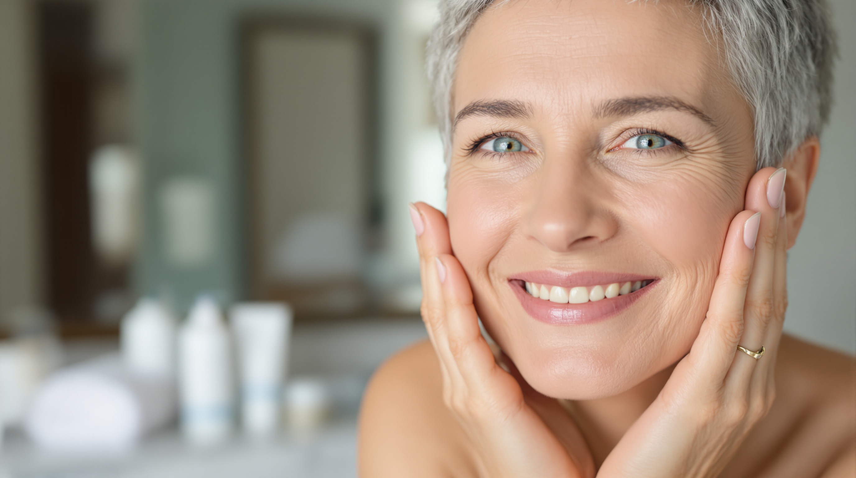 Femme souriante aux cheveux gris courts touchant son visage, avec un arrière-plan flou de salle de bain.