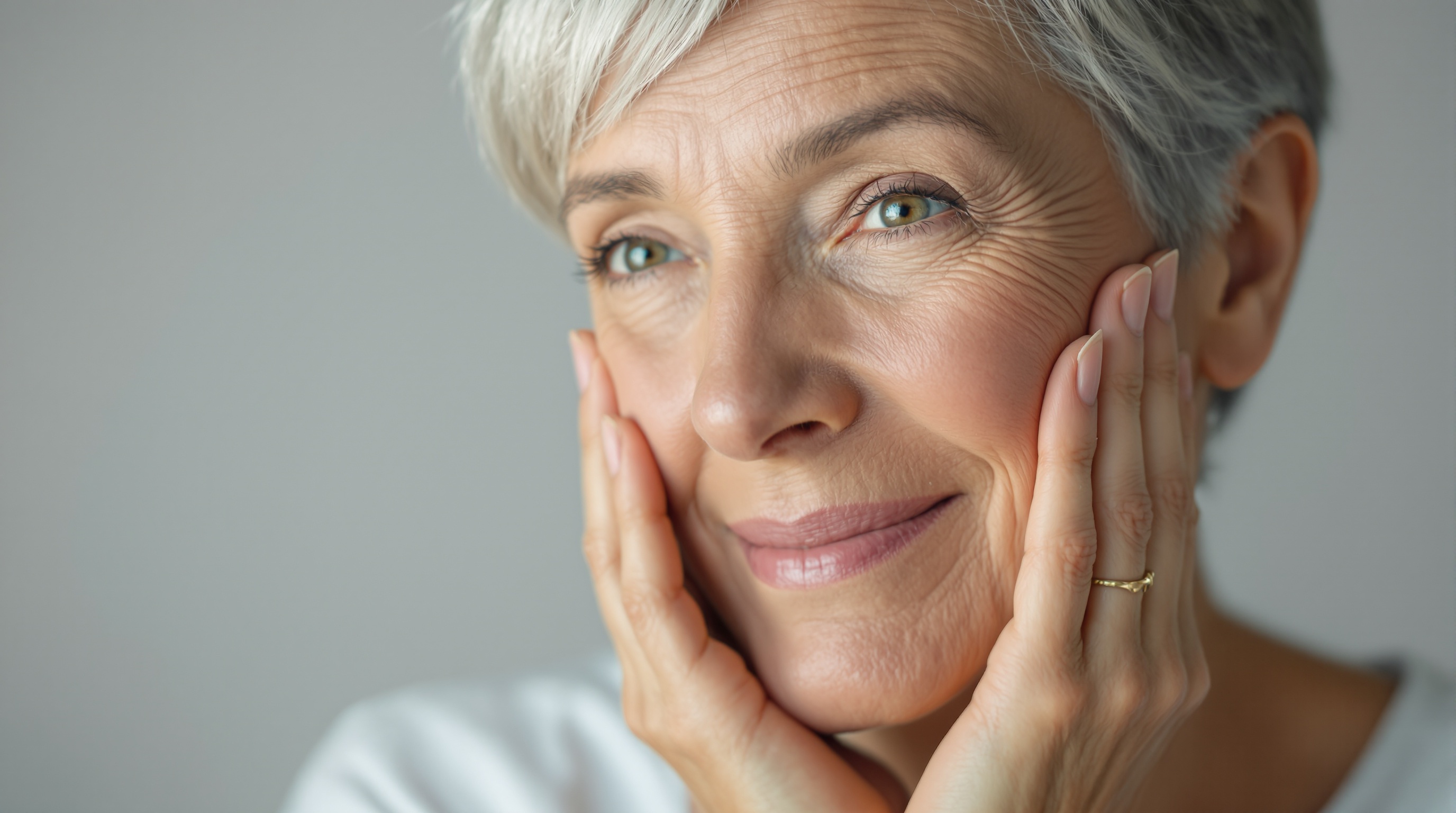 Femme âgée aux cheveux gris souriant doucement, tenant son visage avec les deux mains.
