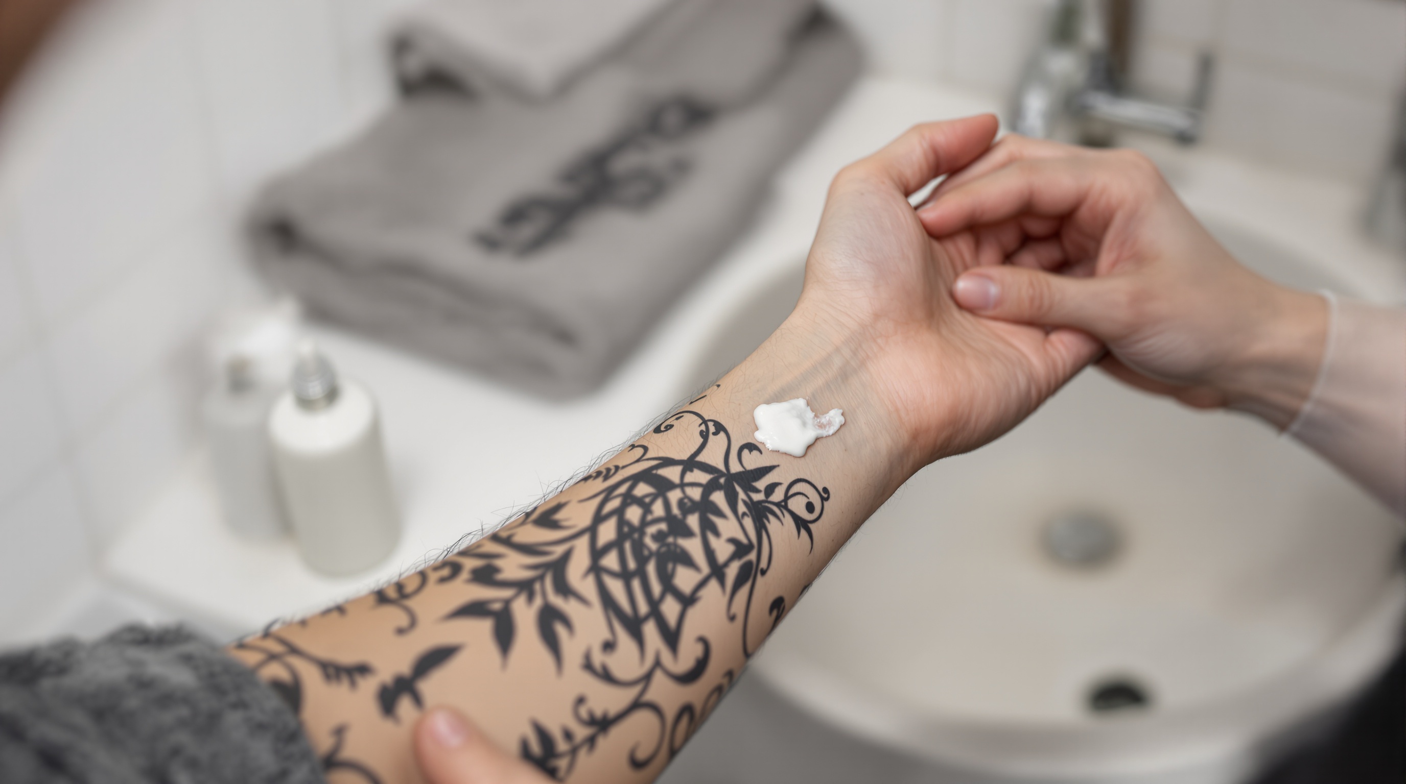 Une personne applique de la crème sur un tatouage noir complexe situé sur l’avant-bras.